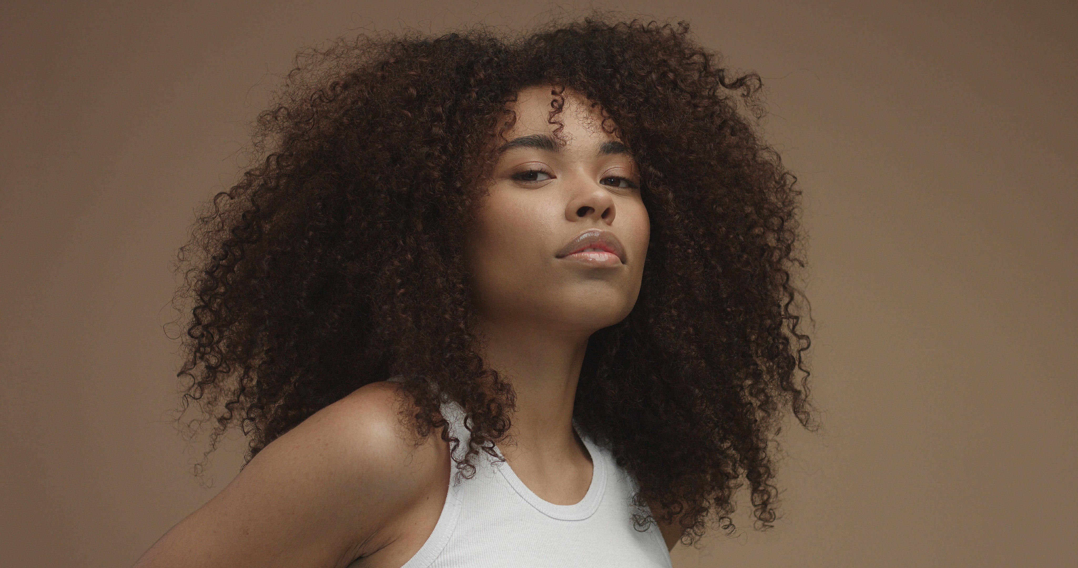 mixed-race-black-woman-portrait-with-big-afro-hair-curly-hair-beige-background.jpg